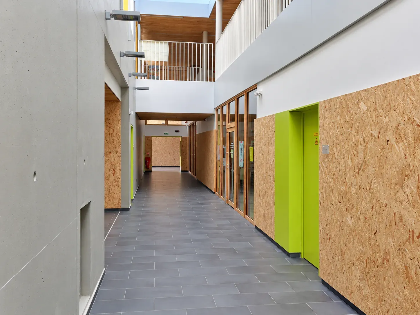 Circulation intérieure du collège de Nieppe, panneaux en bois brut, portes colorées et sol en carrelage gris