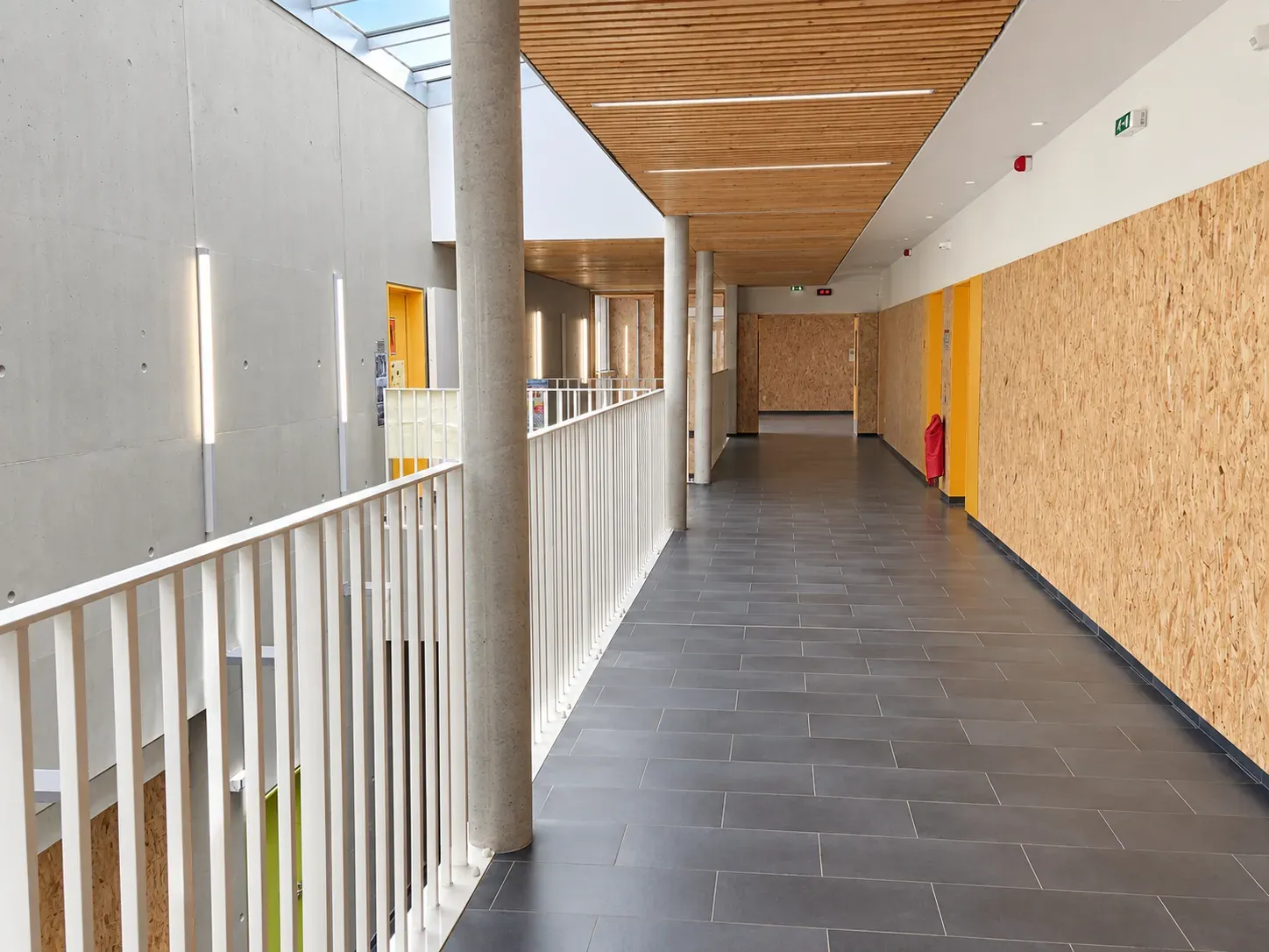 Coursive du collège de Nieppe avec garde-corps blanc, poteaux en béton et plafond en lames de bois