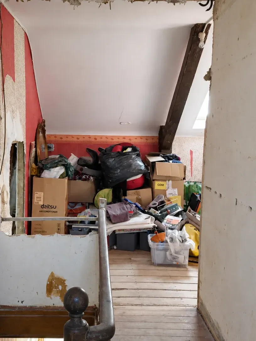 Palier d'étage sous combles avant rénovation, murs bruts, cartons et ancienne rampe d'escalier
