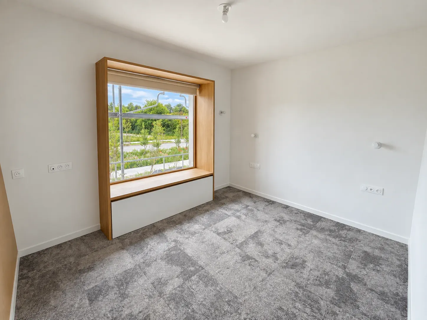 Chambre d'hôtel hospitalier avec grande fenêtre en niche en bois et moquette grise