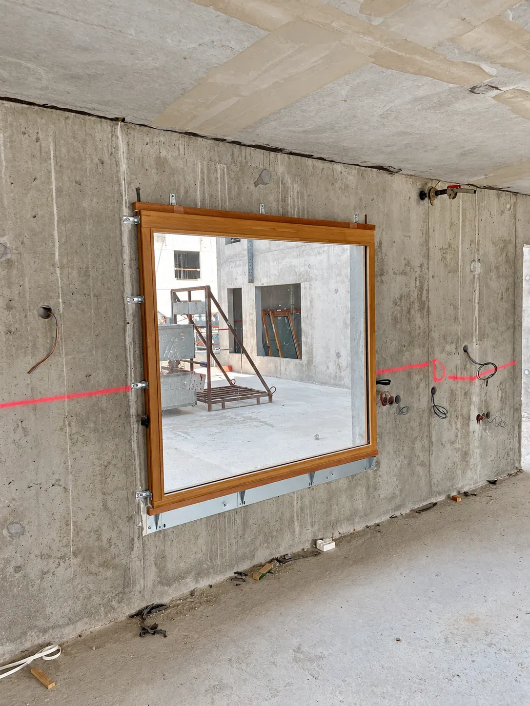 Fenêtre en bois posée dans un mur en béton brut, avec un repère laser