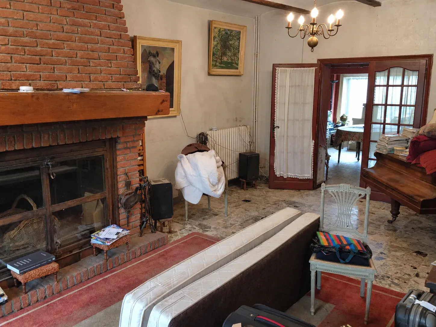 Pièce de vie avant rénovation avec cheminée en briques, ancien mobilier et sol usé