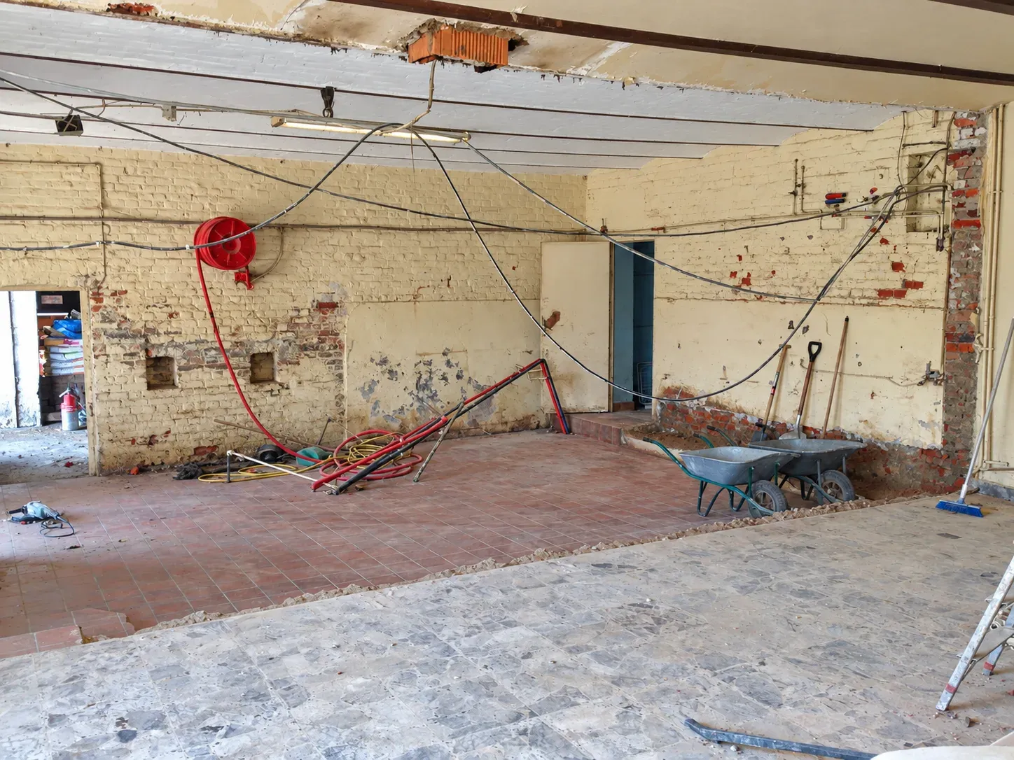 Pièce en cours de dépose, murs en briques mis à nu, réseau électrique apparent et ancien sol